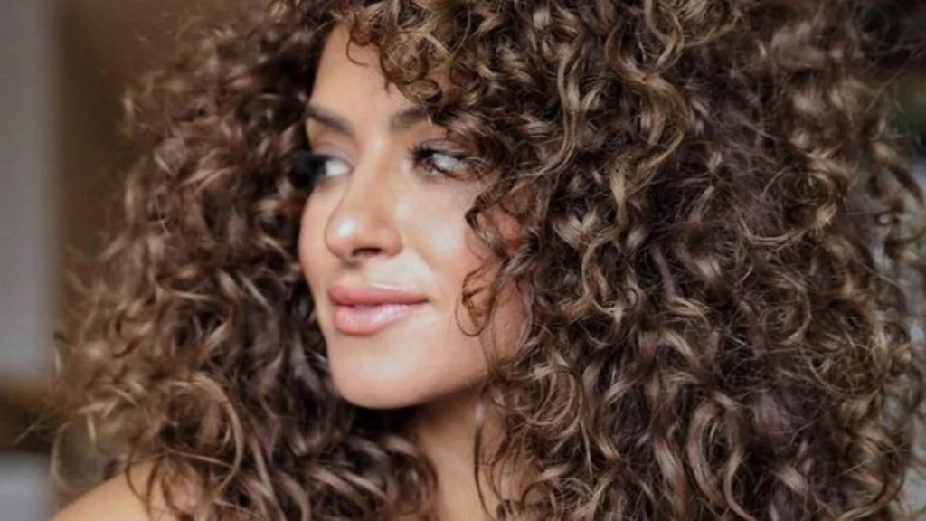Mujer de perfil con una melena voluminosa de pelo rizado y castaño.